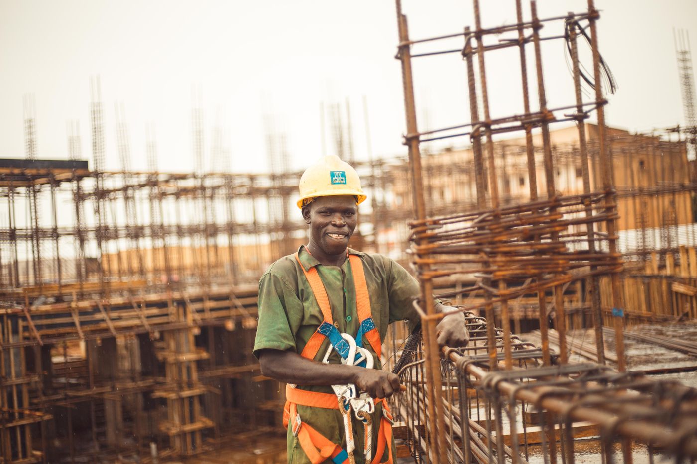 Un ouvrier souriant sur un chantier, casque jaune et harnais